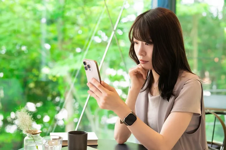 カフェでスマートフォンを真剣な表情で見つめる30代女性。婚活サービス選びに悩む様子を表現したイメージ