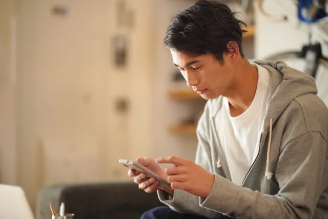 仮交際終了の連絡を受け、自宅のソファでスマートフォンを見ながら考え込む婚活中の男性