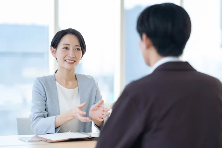 結婚相談所のカウンセリングルームで、穏やかな笑顔のカウンセラーが男性に丁寧に説明している様子