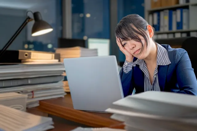仕事に追われて夜遅くまで残業し、パソコンに向かう30代独身女性。結婚に踏み出せず疲れた表情を浮かべている。