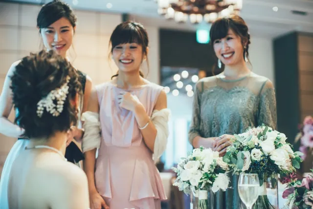 結婚式の高砂席で新婦と談笑するゲストを横目に、少し冷めた表情で新婦を見つめる30代独身女性。