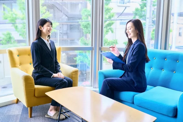 結婚相談所のソファーでアンケート用紙を持った仲人カウンセラーからカウンセリングを受ける34歳独身女性。