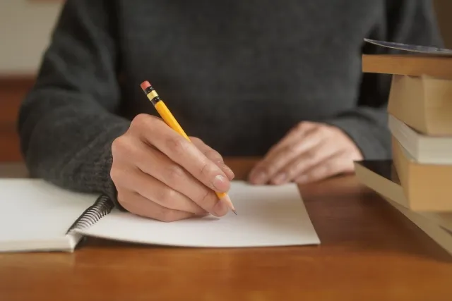 自宅の机でノートを取りながらお見合い勉強をする東大卒エリート男性のイメージ写真