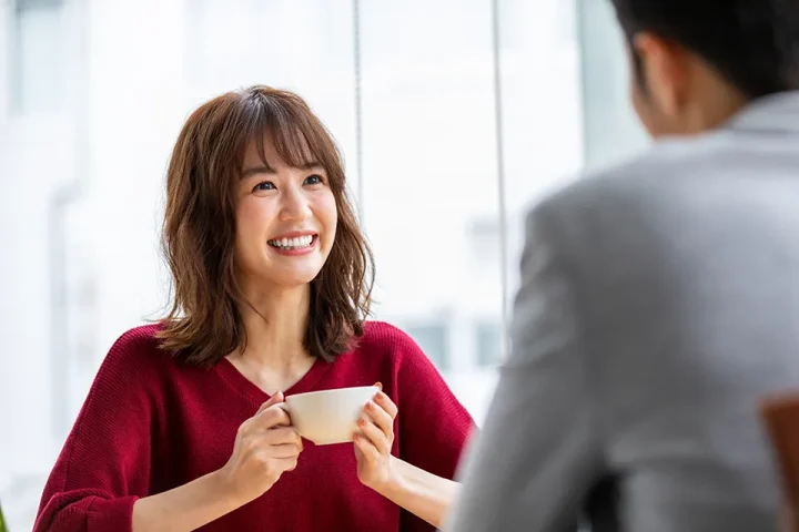 お見合いの流れ｜30代男女が落ち着いたカフェで対面し、女性がティーカップを持って微笑む様子