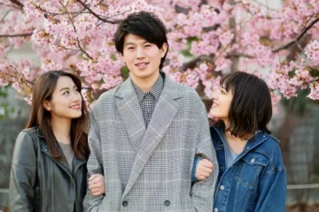 満開の桜を背景に、若い男性の両腕に寄り添う2人の女性が写っている写真