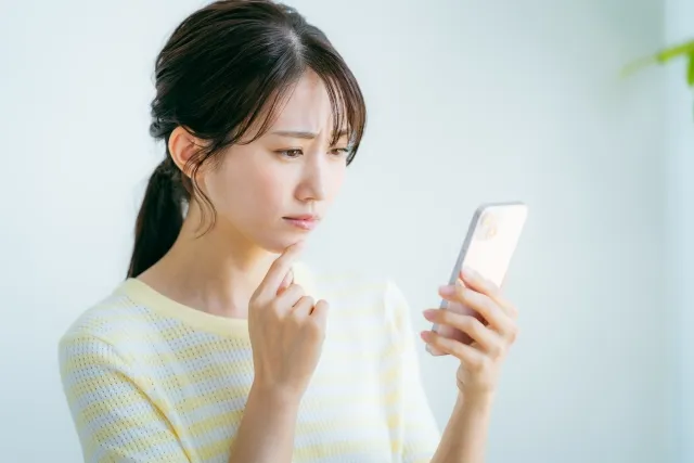 スマホを見つめながら悩んだ表情を浮かべる女性の横顔。真剣交際の切り出しに迷う婚活中の不安や慎重な判断を象徴するイメージ