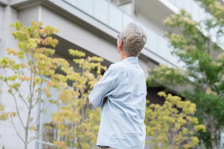 持ち家のマンションを見上げながら、再婚に向けて住まいについて思案する50代男性の姿