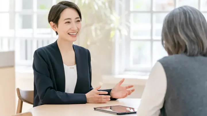 60代女性がカウンセラーに相談をしている背中越しの様子