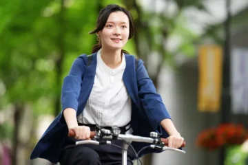 緑道を自転車で走るビジネスカジュアルの女性（エコ通勤・環境配慮）