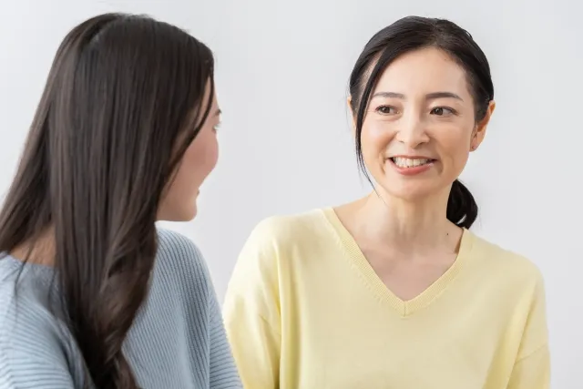 母親が優しく語り掛け、娘が振り向く後ろ姿の母娘。親がそっと背中を押す温かいサポートを表現した写真