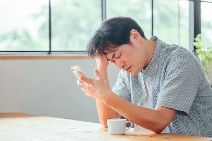 スマートフォンを見て悩む男性