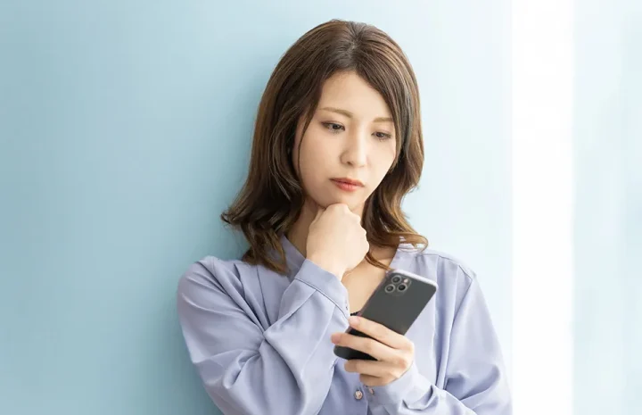 仮交際終了の連絡を受けて戸惑う婚活中の女性。スマートフォンを見つめながら不安そうな表情を浮かべている