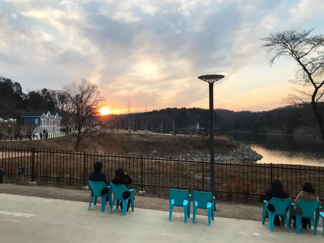 夕日に照らされた宮沢湖の湖畔ベンチで寄り添うカップルの後ろ姿。北欧風の建物と自然が調和する、静かな癒しの空間