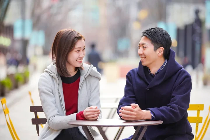 婚活中の男女がテラス席で向き合い、穏やかな笑顔で会話する様子。柔らかい光に包まれた優しい雰囲気が、心の距離の近さを感じさせる