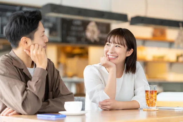 カフェで向かい合って笑顔で話す男女のカップル。共働きや支え合う関係性を象徴する婚活イメージ