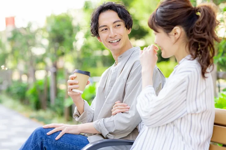 30代の男女が緑豊かな公園のベンチで向かい合い、穏やかな笑顔で会話する様子。価値観を共有しながら理想の未来を描く婚活イメージ