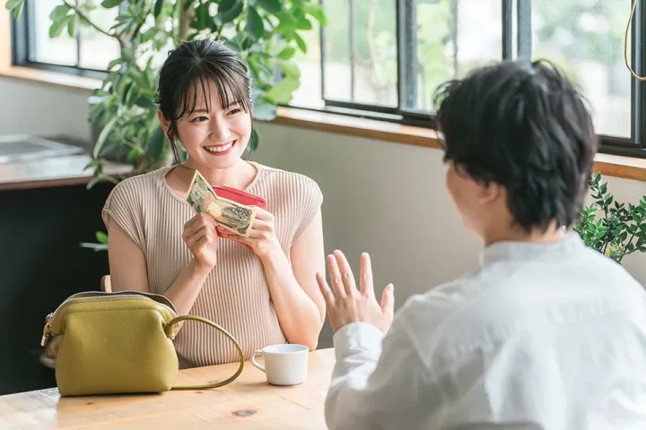 女性が仮交際中のデートでテーブル席にて財布からお札を出して支払いをしようとしている様子