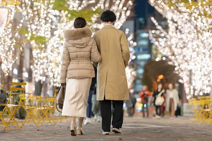 イルミネーションの道を腕を組んで歩くカップルの後ろ姿。恋愛のときめきや非日常感を象徴するイメージ。
