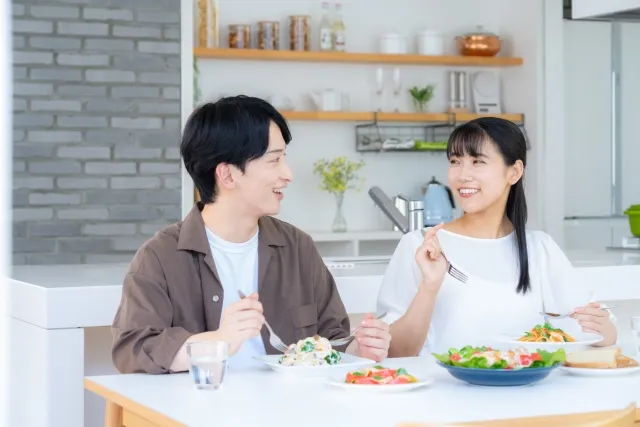 明るいリビングで並んで食事をしながら会話する夫婦の写真。結婚生活の協力や安心感を象徴するイメージ。