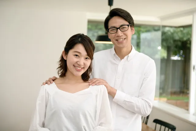 明るい室内で笑顔を交わす30代カップル。男性が女性の両肩に優しく手を添え、信頼と安心感が伝わる一枚