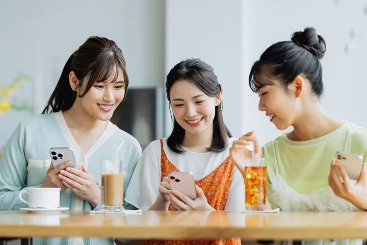 婚活について友人同士がカフェでスマホ画面を見ながら話し合う女性たち