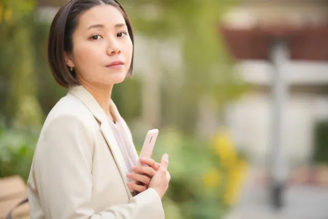 スマホを手に立ち止まり、少し迷いながらも前を向いて未来を考える婚活中の女性のイメージ写真