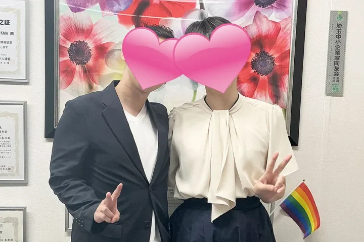 20代カップルの成婚退会手続き風景。ハートで顔を隠しながらも、笑顔でピースサインをする幸せそうなツーショット写真。