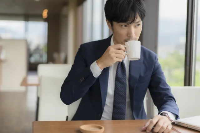 カフェの窓際で、30〜40代の男性がコーヒーを飲みながら穏やかな表情で外を眺めている様子。