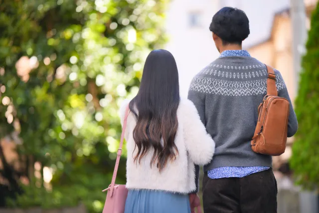 結婚を前提に付き合う30代・40代カップルが晩秋の緑道を腕を組んで歩く後ろ姿