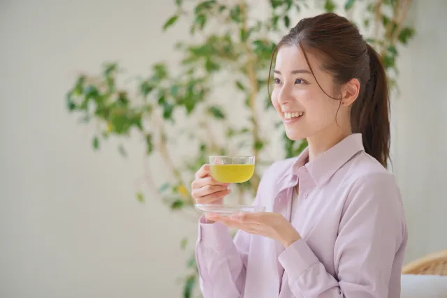 ソファーに座り、グラスを手に笑顔で相手の話を聞く女性の横顔。自然なリアクションと聞き上手な雰囲気が伝わる写真