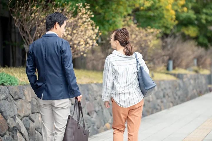 緑豊かな公園の道を並んで歩く40代カップルの後ろ姿。目を合わせながら楽しそうに会話している様子