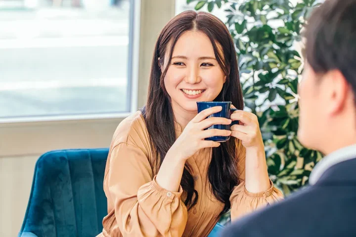 初デートの会話中、女性が笑顔でコーヒーカップを持ちながら男性から視線を外している様子。会話は続いているがどこか噛み合わない“すれ違い”を感じさせるシーン。
