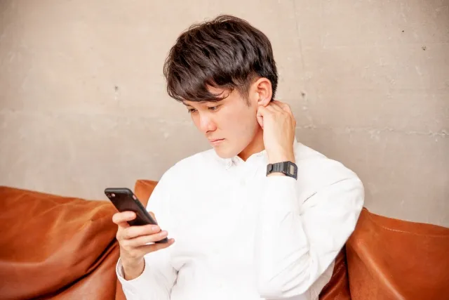 スマホ画面を見て困った表情を浮かべる男性。婚活アプリの使い方や進め方に迷い、不安を抱えている様子を表現したイメージ写真。