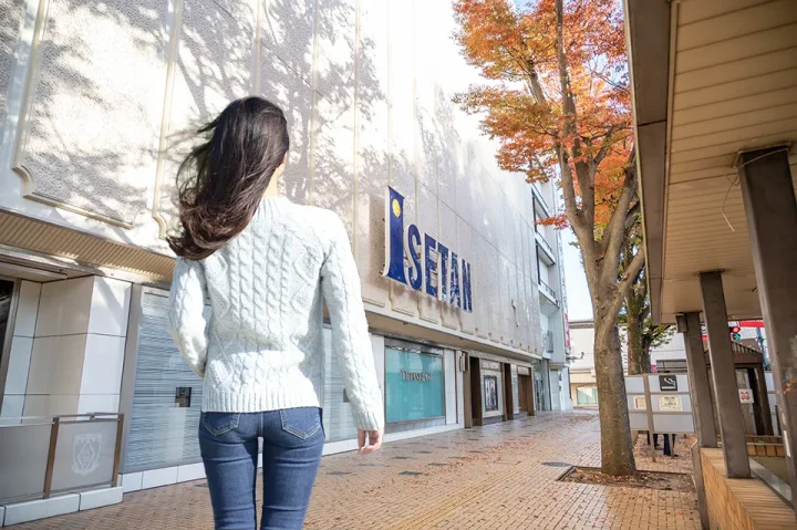 浦和駅前を歩く女性の後ろ姿。忙しい女性が前向きに婚活を始めるイメージ。伊勢丹前の明るい昼間の風景。