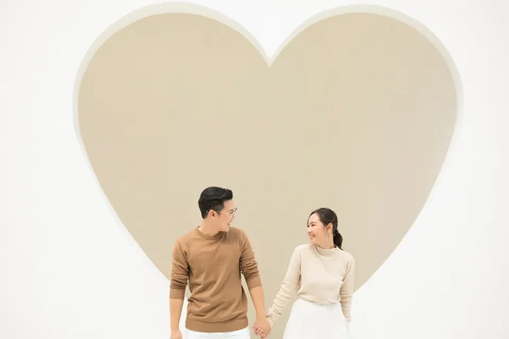 ハート背景の前で手をつなぎ、見つめ合うカップルの婚活イメージ写真