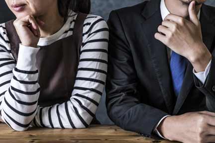 テーブルで隣り合わせに座る夫婦。互いにそっぽを向き、気まずい空気が漂う様子。