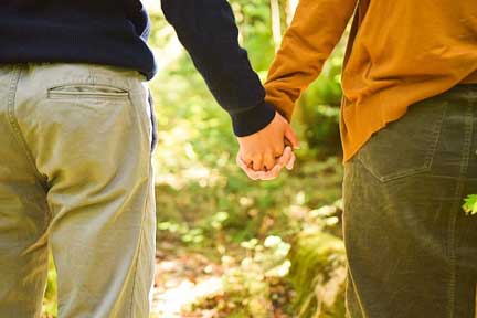 自然豊かな緑の中を手をつなぎ歩くカップルの後ろ姿の写真