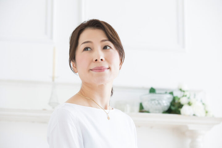 婚活に向き合う品のあるアラフォー女性が、明るい室内で未来を見つめるように斜め上を見つめている様子