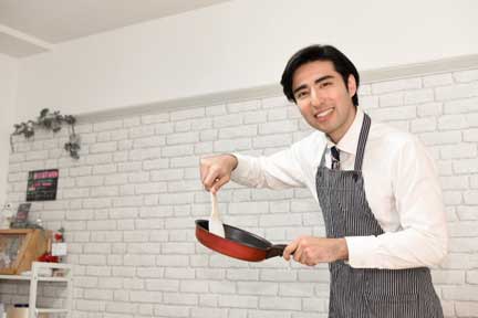 にこやかな表情でフライパンで調理するエプロン姿の男性