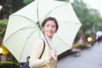 淡い緑色の雨傘をさす女性が振り向く風景