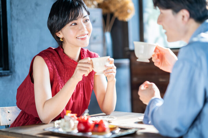 カフェでコーヒーを飲みながら笑顔で会話するカップル。リラックスした雰囲気の中で、将来のパートナー像をイメージできる写真。