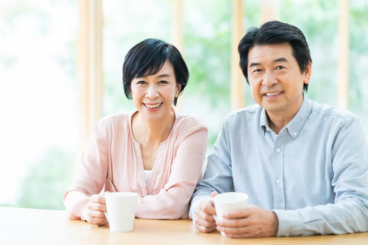 テーブルで寄り添いながらお茶を飲む50代カップルの穏やかな会話シーン