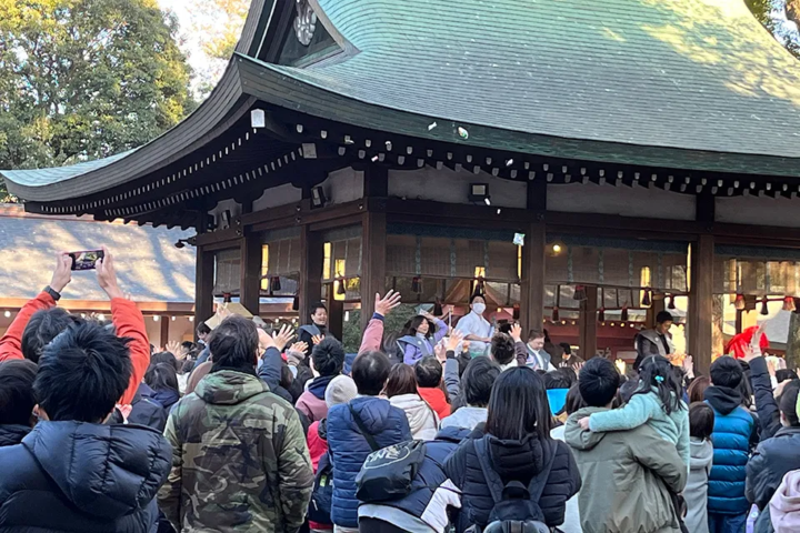 如月会の会員が舞殿から福豆をまき、周囲の参拝者が手を伸ばして受け取ろうとしている節分祭の様子